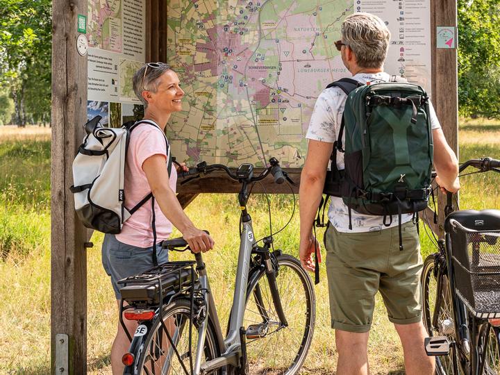 Urlaubsgäste planen Ihre Fahrradroute bei dem Wanderschild.