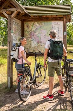 Urlaubsgäste planen Ihre Fahrradroute bei dem Wanderschild.