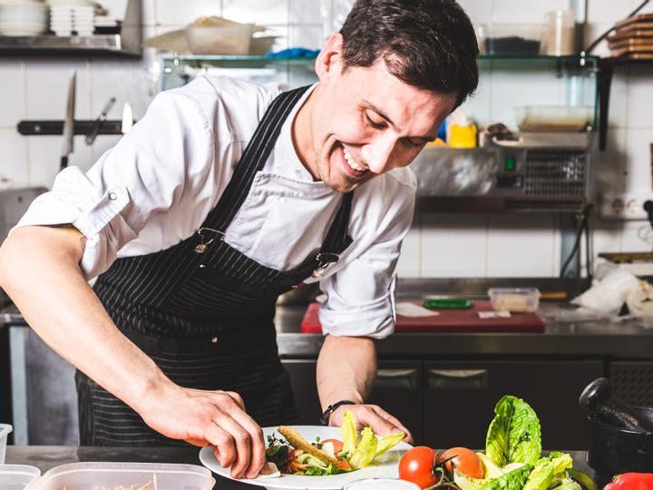 Koch steht in der Küche, lächelt und bereitet einen Salat zu.