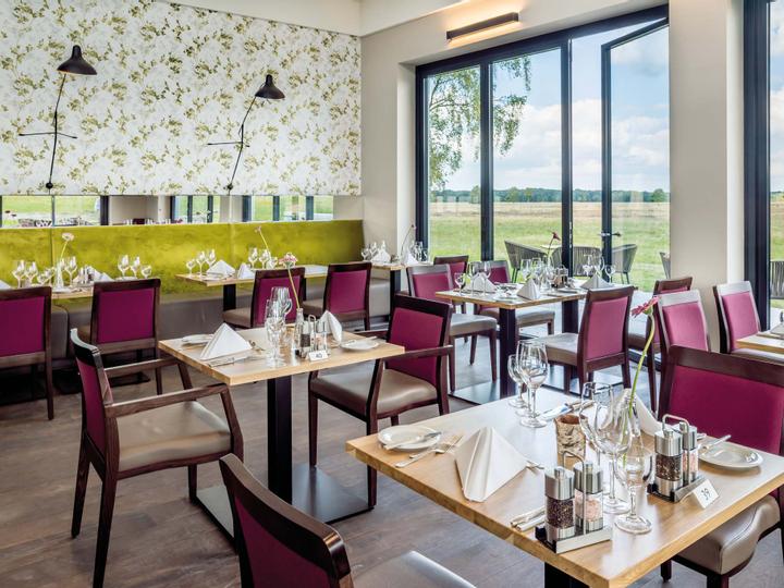 Mehrere kleine Restauranttische in hellem Raum mit Blick in die Natur