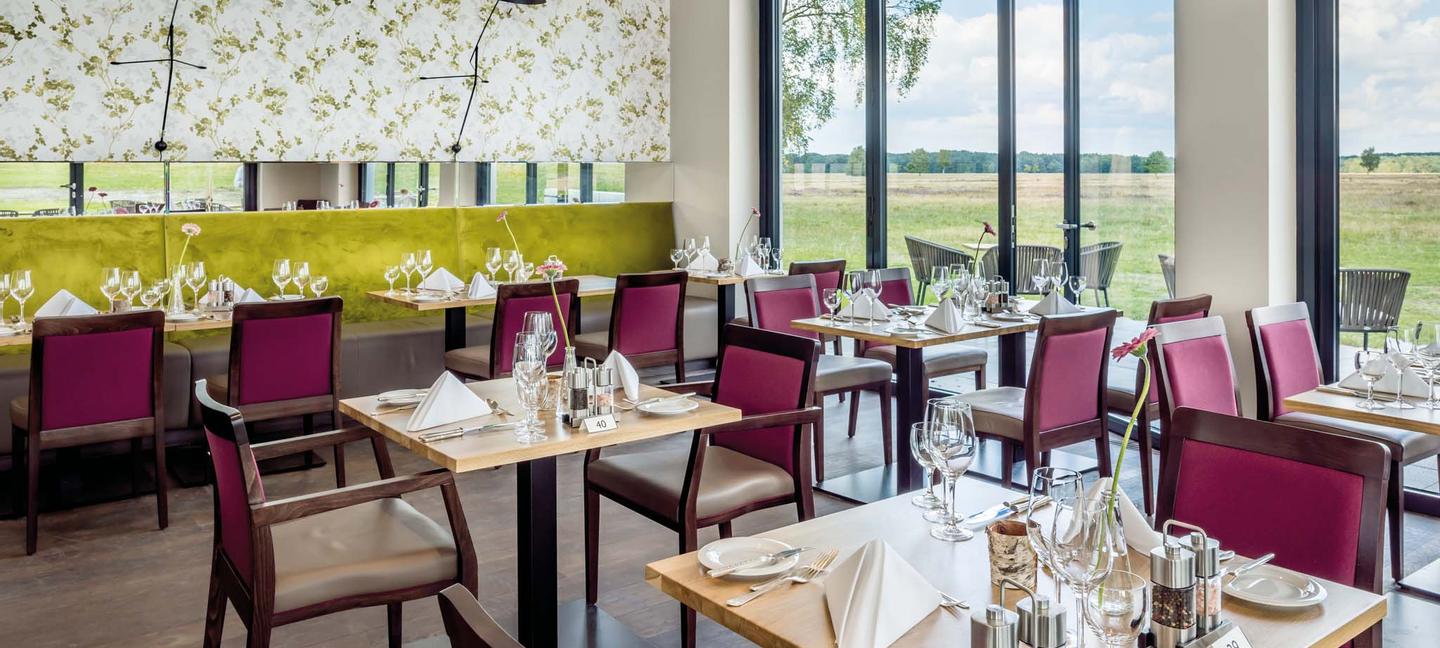 Mehrere kleine Restauranttische in hellem Raum mit Blick in die Natur